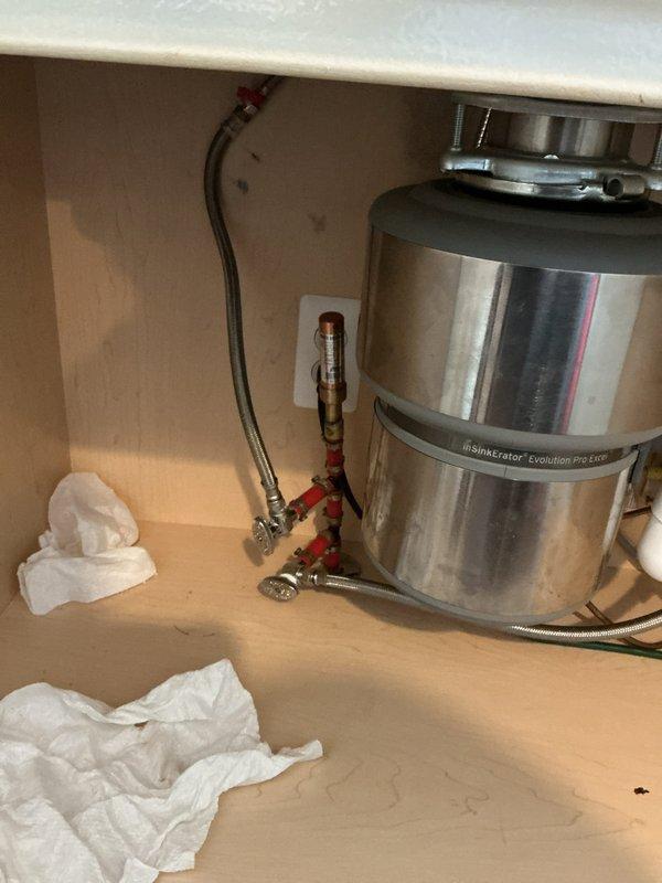 Responded to kitchen sink water leak complaint. Upon inspection, accessed cabinet space beneath sink and examined garbage disposal unit and associated plumbing connections. Identified leak source at braided supply line connections with red valve handles. Tightened compression fittings on flexible supply hoses and verified all mounting hardware and drain connections were secure. Tested system for proper operation and confirmed leak was resolved with no further water discharge observed.