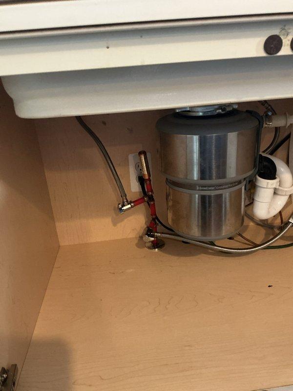 Responded to kitchen sink water leak complaint. Upon inspection, accessed cabinet space beneath sink and examined garbage disposal unit and associated plumbing connections. Identified leak source at braided supply line connections with red valve handles. Tightened compression fittings on flexible supply hoses and verified all mounting hardware and drain connections were secure. Tested system for proper operation and confirmed leak was resolved with no further water discharge observed.