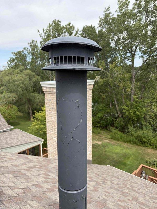 Completed installation of black metal chimney cap on roof vent following tankless water heater installation at two-story residence. Accessed rooftop using extension ladder to properly cap the venting system from the 3-year-old tankless unit located in basement. Secured new double-walled metal cap with rain hood to existing chimney pipe structure, ensuring proper ventilation while preventing water intrusion. Verified PVC venting connections in basement remained intact and properly supported within ceiling joists. All work completed to code specifications for tankless water heater exhaust systems.