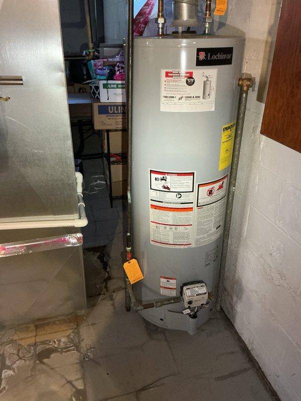 Responded to water leak in basement of 70-year-old residence that had been ongoing for two weeks. Upon inspection, identified the source as a cracked condensate pump rather than the hot water heater initially suspected by homeowner. Inspected Lochinvar water heater unit and surrounding utility area, documenting moisture damage on concrete floor and verifying condensate drainage system. Photographed affected areas showing water staining patterns on floor extending from equipment location and white plastic drain pan with visible discharge tubing. Confirmed diagnosis of failed condensate pump requiring replacement to resolve ongoing water leak issue.