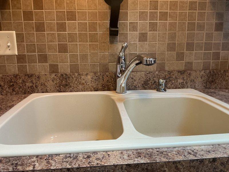 Installed customer-supplied chrome pull-out kitchen faucet with matching soap dispenser on double-basin undermount sink with granite countertop. Verified all supply line connections, tested faucet operation and spray function, confirmed proper drainage, and ensured no leaks at mounting points or under-cabinet connections.