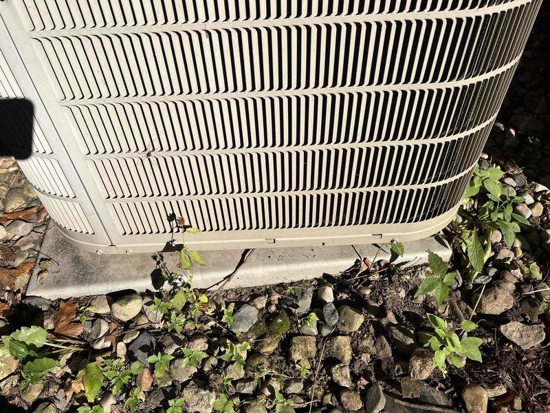 Responded to service call for outdoor condensing unit evaluation. Upon arrival, confirmed unit bears flame stickers indicating previous installation, though installer verification was requested. Conducted level assessment of approximately 2007-vintage air conditioning condenser positioned on concrete pad in basement area. Using precision digital level instrument, measured unit alignment and documented 74°F ambient temperature reading during inspection. Observed condensing unit sitting on concrete base with surrounding ground cover including rocks, soil, and vegetation encroachment. Photographically documented current installation conditions, including unit positioning, concrete pad status, and level measurements. Confirmed condenser is not properly leveled on existing pad. Provided assessment findings and discussed restoration options to properly level equipment for optimal performance and longevity.