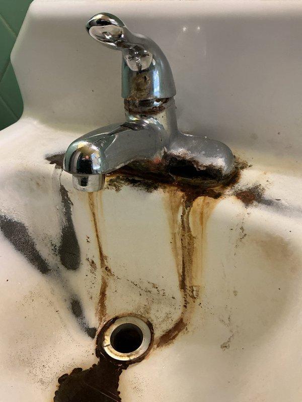 Removed and replaced deteriorated pedestal sink and faucet assembly per customer estimate. The existing wall-mounted sink exhibited extensive rust staining, corrosion around fixtures, and damaged porcelain along the mounting edge. Disconnected water supply lines and removed old chrome-plated faucet with separate hot and cold handles. Detached compromised sink from wall mounting, ensuring proper care around vintage mint green diagonal tile work and black tile wainscoting. Installed new pedestal sink unit with updated chrome faucet assembly. Connected hot and cold water supply lines, tested for leaks, and verified proper drainage. All fixtures secured and operational upon completion.
