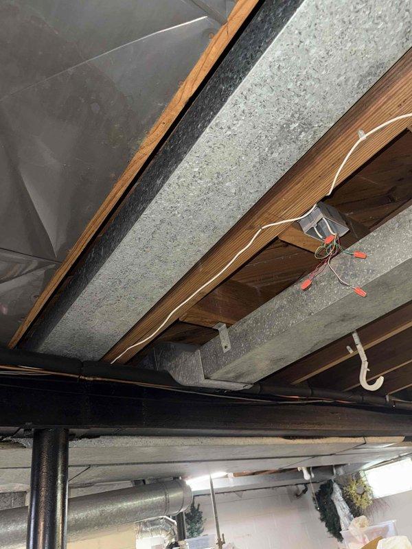 Responded to no cooling complaint on 11-year-old air conditioning system with intermittent Nest thermostat operation. Performed diagnostic evaluation of thermostat wiring and connections in attic space. Inspected low voltage control wiring between thermostat and air handler, examining wire terminations and routing through structural framing. Assessed thermostat compatibility with existing HVAC equipment and verified proper C-wire installation for consistent power supply to smart thermostat. Evaluated condensing unit operation and communication with indoor equipment. Documented existing wiring configuration and equipment conditions through photographic evidence showing thermostat wire routing through floor joists and proximity to ductwork system.