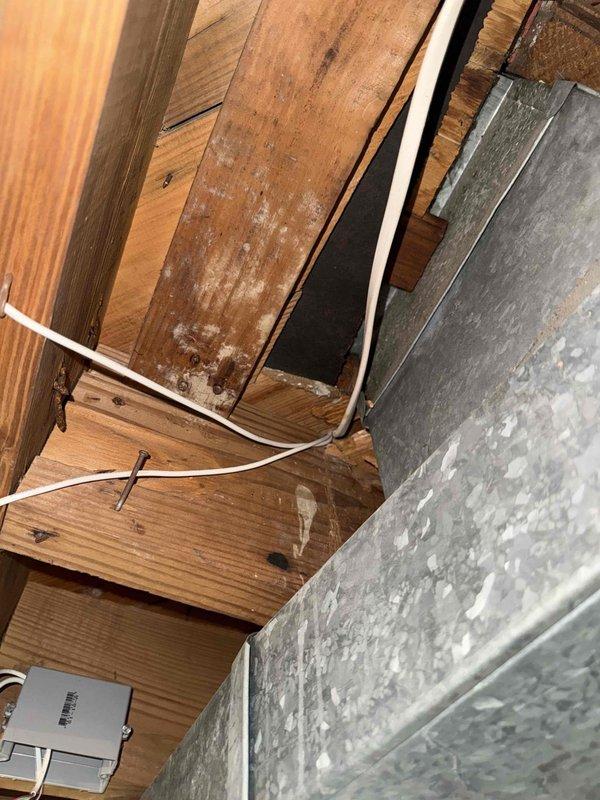 Responded to no cooling complaint on 11-year-old air conditioning system with intermittent Nest thermostat operation. Performed diagnostic evaluation of thermostat wiring and connections in attic space. Inspected low voltage control wiring between thermostat and air handler, examining wire terminations and routing through structural framing. Assessed thermostat compatibility with existing HVAC equipment and verified proper C-wire installation for consistent power supply to smart thermostat. Evaluated condensing unit operation and communication with indoor equipment. Documented existing wiring configuration and equipment conditions through photographic evidence showing thermostat wire routing through floor joists and proximity to ductwork system.