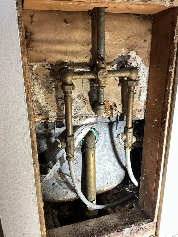 Conducted complimentary on-site consultation to provide second opinion on existing plumbing installation. Assessed exposed piping assembly in wall cavity featuring brass copper pipe configuration with multiple valves and fittings connected to central black drain/vent stack, along with water heater component showing flexible supply lines. Documented conditions via photographs for reference and recommendation purposes.