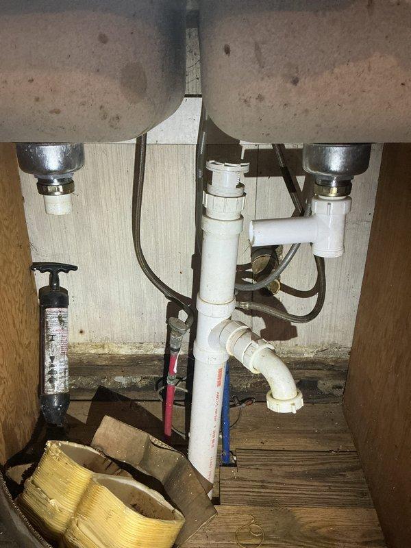 Conducted comprehensive plumbing assessment for drain pipe replacement and repair at residential property involving kitchen sink, bathroom tub, and toilet systems. Inspected dual-basin stainless steel kitchen sink with partially disassembled faucet assembly, noting deteriorated condition with significant mineral deposits and drainage concerns. Evaluated under-sink plumbing configuration including white PVC drain assembly with chrome drain baskets, vertical drain pipe connections, flexible hoses, and inline water filtration component. Documented existing infrastructure condition, wear patterns, and necessary repairs to provide accurate estimate for drain line replacement and fixture restoration across multiple bathroom and kitchen locations.