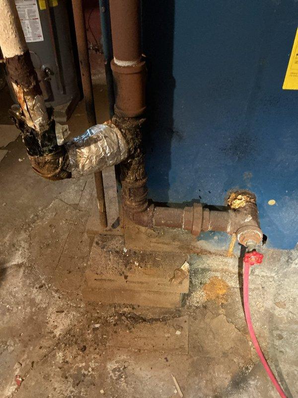 Responded to service call regarding potential drainage issues and deteriorating boiler system piping. Upon inspection, identified severely corroded cast iron pipes in the mechanical system with visible rust deterioration and compromised pipe integrity. Documented extensive corrosion on heating system components, including multiple pipe joints showing advanced oxidation and temporary metallic tape repairs indicating previous leak attempts. Assessed drainage line conditions and prepared camera inspection equipment as requested by homeowner to evaluate main drain line leading to municipal connection. Photographed damaged interior wall areas showing evidence of previous water intrusion and active renovation work, along with exposed plumbing infrastructure. Confirmed boiler piping system requires immediate attention due to corrosion-related failures and potential perforation points throughout the cast iron pipe network.