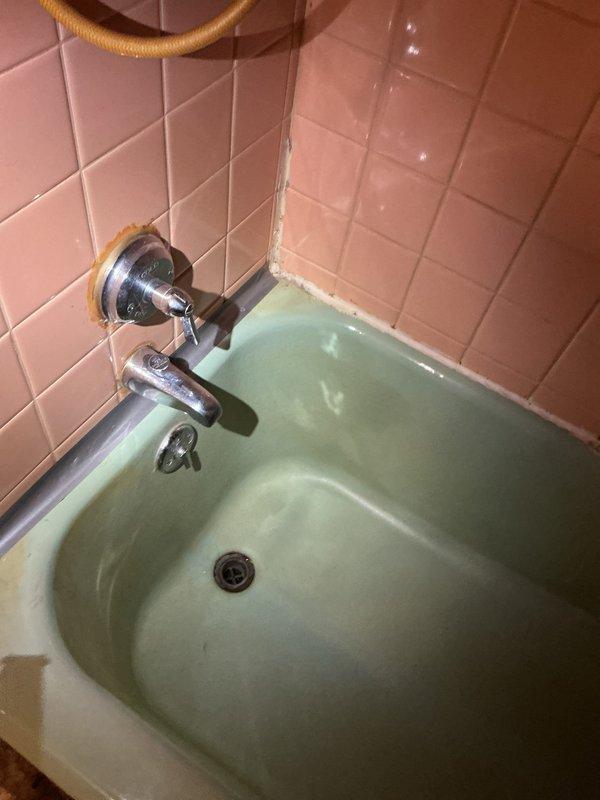 Responded to service call for leaking bathtub faucet with chrome finish mounted on pink tile surround. Upon inspection, identified deteriorated valve seats and worn cartridge assembly causing persistent drip from spout. Accessed supply lines through attic crawl space above bathroom, shut off water supply, and replaced faulty internal cartridge components and seals. Addressed compromised caulking and grout at tile corners where water infiltration had occurred. Tested faucet operation post-repair to confirm leak elimination and proper water flow. Restored water supply and verified no additional leaks at connections or fixture mounting points.