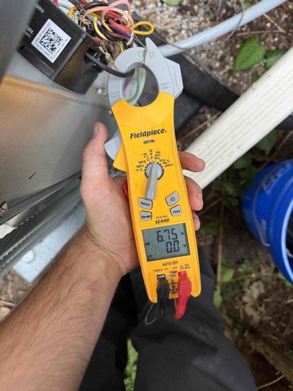 Responded to no cooling complaint on six-year-old air conditioning system. Upon arrival, performed electrical diagnostics using clamp meter to measure amperage and voltage at outdoor unit. Inspected capacitor connections and verified proper wire terminations at dual run capacitor terminals. Measured compressor and condenser fan motor amperage draws to determine operational status of components. All electrical connections were secure with brown, white, and yellow wires properly terminated at capacitor. System evaluated and measurements documented for diagnostic purposes.