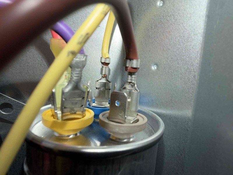 Responded to no cooling complaint on six-year-old air conditioning system. Upon arrival, performed electrical diagnostics using clamp meter to measure amperage and voltage at outdoor unit. Inspected capacitor connections and verified proper wire terminations at dual run capacitor terminals. Measured compressor and condenser fan motor amperage draws to determine operational status of components. All electrical connections were secure with brown, white, and yellow wires properly terminated at capacitor. System evaluated and measurements documented for diagnostic purposes.