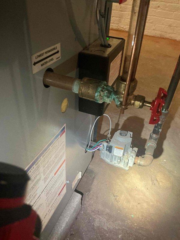 Completed return visit to address leaking and corroded piping on 5-year-old boiler system located in basement. Replaced deteriorated galvanized steel pipe sections showing active leaks and rust damage with new components including two 3/4" bushings, 3/4" shut-off valve, and multiple 3/4" nipples. Removed heavily corroded brass fittings and reinstalled plumbing assembly with proper threading and sealing to eliminate water intrusion. System tested under pressure following repairs with no leaks detected. Boiler remained operational throughout service and continues providing heat. Floor area beneath repaired section showed evidence of previous water damage from leaking pipes, which has now been resolved with replacement components.