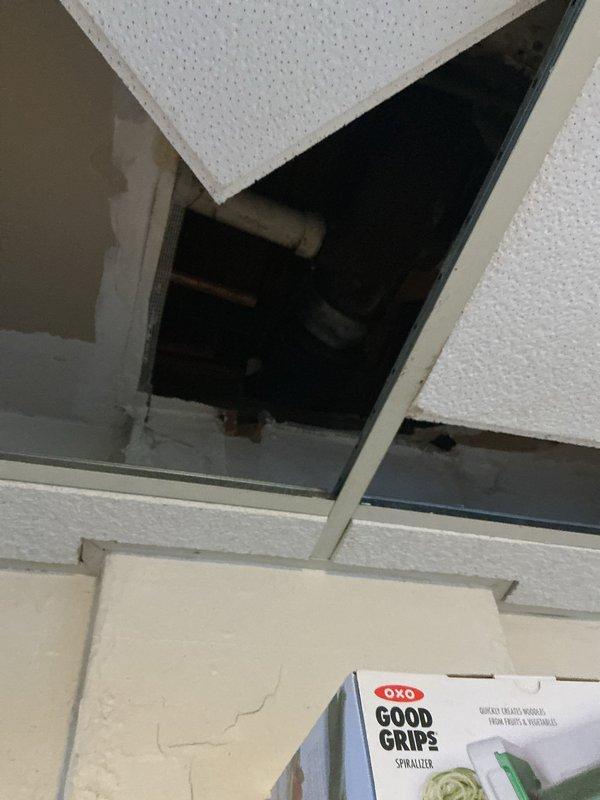Responded to reported stack pipe leak in residential property. Upon investigation, accessed ceiling cavity through drop ceiling system in kitchen area and inspected plumbing stack penetration. Found active leak at stack pipe connection point with evidence of water intrusion causing damage to surrounding structural components. Further inspection revealed water damage extending to fireplace area with deterioration of wooden framing members and visible moisture staining on exposed materials. Documented conditions with photographic evidence showing compromised ceiling tiles, exposed piping in ceiling cavity, and water-damaged fireplace framing with signs of prolonged moisture exposure. Identified source of leak at defective stack pipe joint requiring repair or replacement to prevent further water damage to structure.