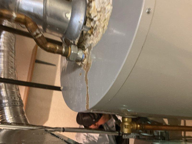 Responded to service call for water leaking from furnace in basement with suspected condensate pump failure. Upon inspection, discovered significant water damage and mineral deposits on water heater tank and surrounding pipe connections, indicating long-term leak issues at tank junction points. Assessed HVAC system and prepared for customer-supplied Nest thermostat installation to replace existing unit.