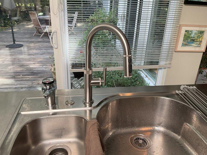 Completed installation of stainless steel double-basin kitchen sink with modern pull-down faucet in brushed nickel finish and coordinating soap dispenser. Connected all drain assemblies including garbage disposal unit with proper PVC trap configuration, verified all supply line connections, and tested system for proper drainage and leak-free operation.