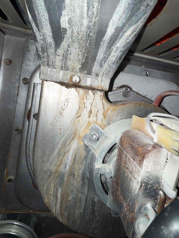 Responded to water leak complaint on 10-year-old air conditioning unit in basement. Upon inspection, discovered significant water staining and discoloration around the evaporator coil area, indicating prolonged moisture exposure. Found primary condensate drain line completely obstructed, causing water to back up and overflow into the living space. Observed corrosion and rust accumulation at the base of the air handler cabinet, consistent with chronic drainage issues. Cleared condensate drain blockage using appropriate tools and verified proper drainage flow. Flushed drain line with cleaning solution to remove biological buildup and debris. Inspected drain pan for cracks or damage; pan structurally sound but showed evidence of standing water. Tested system operation and confirmed condensate draining properly through primary drain line. Advised ongoing maintenance of condensate system to prevent future blockages. Photographed affected areas showing water damage to insulation and corrosio