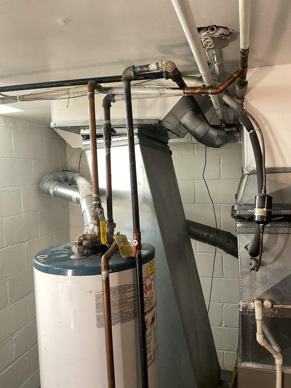 Responded to service call for reported water leak from tanked water heater unit. Upon arrival, accessed mechanical room and conducted thorough inspection of white cylindrical tank-style water heater with associated copper piping assembly and connections. Evaluated unit for source of leak, examined all visible plumbing connections, shut-off valves, and supply lines at top of tank. Inspected tank exterior, pressure relief valve, drain valve, and surrounding floor area for evidence of active water seepage or moisture accumulation.