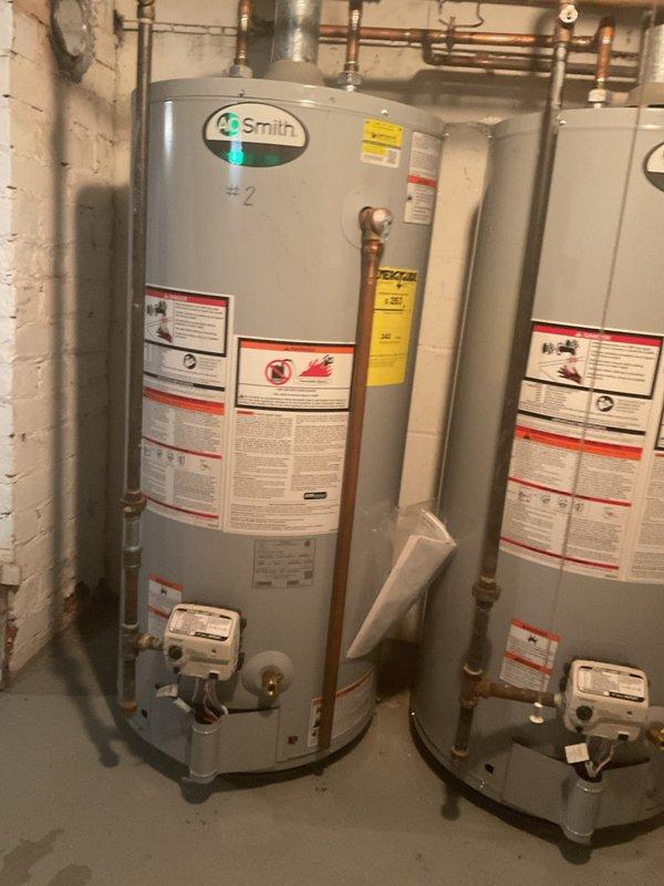Responded to service call for insufficient hot water production from tanked water heater system. Accessed basement utility room through tenant units to inspect dual A.O. Smith water heater installation consisting of units #2 and #3. Performed diagnostic evaluation of both tanked water heaters, examining gas control valves, copper supply and distribution piping, shut-off valves, and overall system configuration. Inspected manufacturer labels, safety warnings, and operational specifications on both units. Assessed piping connections, joints, elbows, and valve assemblies for proper function. Evaluated gas supply system and burner operation to determine cause of inadequate heating capacity. Documented existing installation condition including copper piping patina, insulated pipe runs, and dual-unit configuration designed for high-capacity residential hot water demand.