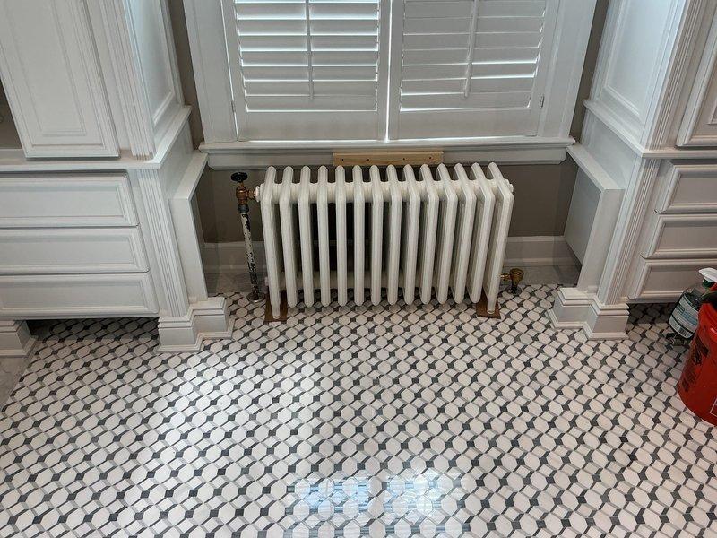 Replaced failed steam traps on cast-iron radiator system in bathroom with 1/2" steam traps sourced from hydronics supply in Ferndale under specified purchase order. Serviced radiator heating unit beneath window, addressing trap failures to restore proper steam heating function and system efficiency.