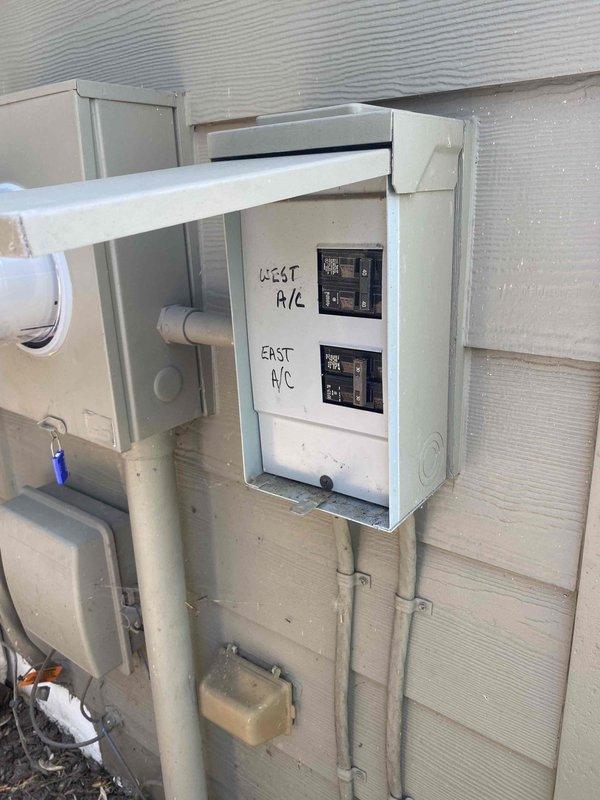 Responded to service call for non-operational air conditioning unit at rear of property. Upon arrival, inspected 20-year-old outdoor AC system that was completely non-functional with no sound or operation. Evaluated electrical disconnects for both west and east AC units, examined breaker panel configuration, and assessed overall system condition. Documented equipment age, electrical connections, and PVC refrigerant line routing. Photographed existing electrical service panels, disconnect switches, and outdoor condenser unit setup to provide comprehensive assessment for full system replacement estimate due to age and failure of equipment.