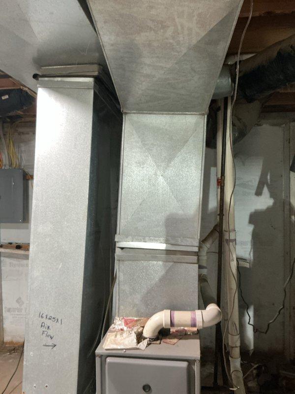 Conducted comprehensive assessment of natural gas heating system in basement of small residential property (0-1500 sq.ft.) to provide replacement estimate. Evaluated existing furnace unit, ductwork configuration including vertical rectangular metal supply duct with visible seams and connections, and associated components including PVC condensate drainage system. Documented current equipment condition, air flow specifications (16x20x1 filter size), electrical panel location, and existing HVAC infrastructure through detailed photographic documentation of mechanical room and upper-level structural spaces to determine optimal replacement unit specifications and installation requirements.
