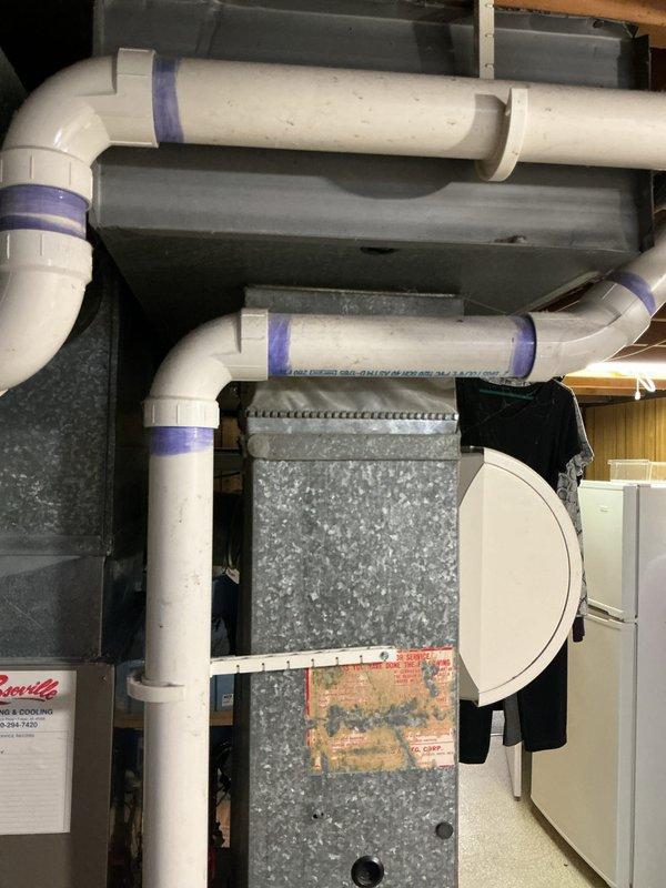 Conducted on-site assessment of existing 6-year-old furnace system located in basement mechanical room to provide replacement estimate. Inspected current equipment configuration including galvanized ductwork connections, PVC condensate drainage system with multiple 90-degree elbows and purple mounting brackets, and surrounding utility space layout. Documented existing HVAC installation with carpeted flooring, white PVC vertical drain lines, and adjacent water heating equipment. Evaluated mechanical room accessibility, existing infrastructure compatibility, and equipment positioning for future furnace replacement planning.