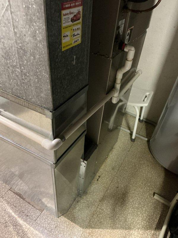 Conducted on-site assessment of existing 6-year-old furnace system located in basement mechanical room to provide replacement estimate. Inspected current equipment configuration including galvanized ductwork connections, PVC condensate drainage system with multiple 90-degree elbows and purple mounting brackets, and surrounding utility space layout. Documented existing HVAC installation with carpeted flooring, white PVC vertical drain lines, and adjacent water heating equipment. Evaluated mechanical room accessibility, existing infrastructure compatibility, and equipment positioning for future furnace replacement planning.