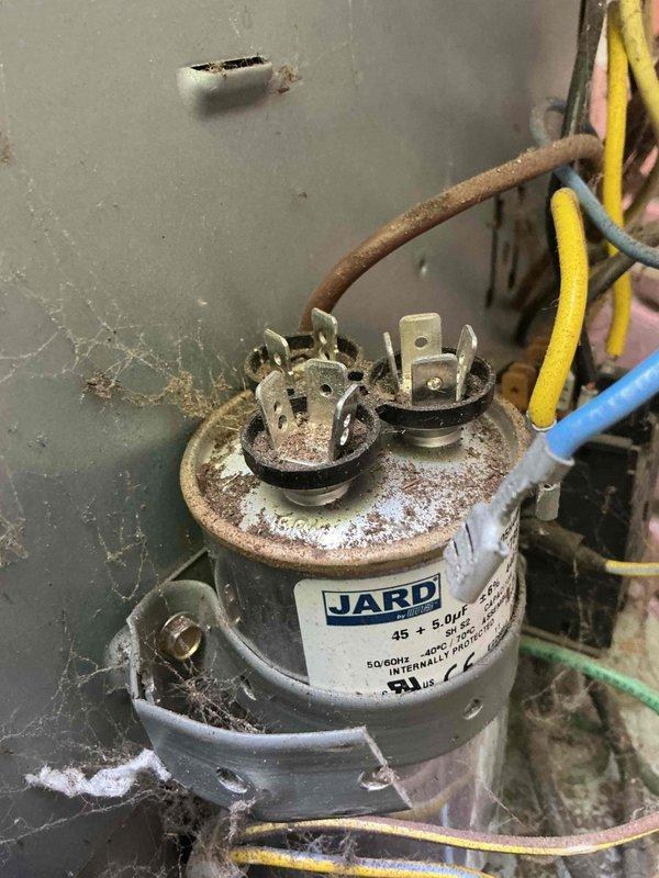 Responded to no cooling complaint on 14-year-old residential air conditioning system. Found outdoor condensing unit not operating due to failed dual-run capacitor showing severe corrosion and rust on housing and terminals. Replaced defective 45+5 μF capacitor with new OEM equivalent, restored power to compressor and condenser fan motor, and verified proper system operation with normal cooling performance.