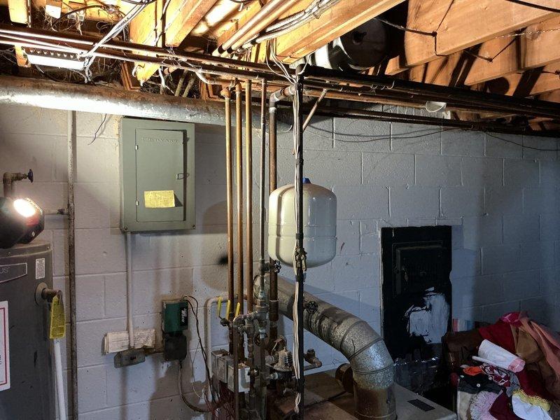 Responded to service call for basement pipe leak assessment following previous contractor's shutdown of basement access. Conducted thorough inspection of basement utility area, examining exposed copper gas lines, plumbing infrastructure, and mechanical systems throughout the space. Documented current condition of all visible piping, including vertical copper runs, valves, fittings, expansion tank, and pressure tank installations along cinder block walls. Inspected ceiling-mounted pipes running between floor joists, identifying copper and metal pipes requiring evaluation. Assessed basement accessibility and provided photographic documentation of existing plumbing system status to facilitate accurate estimate preparation for necessary repairs.