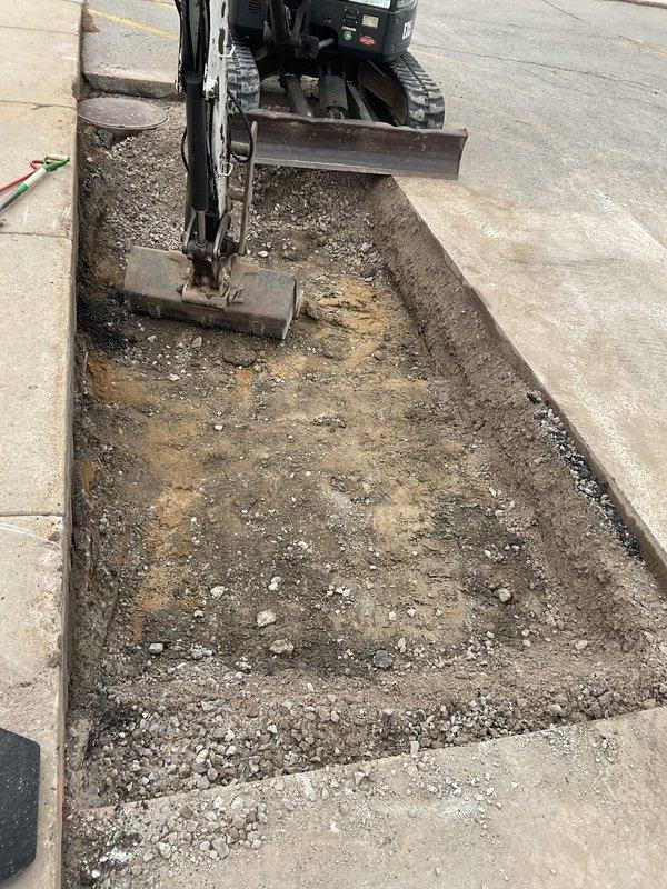 Responded to Miss Dig ticket #2026082605365 for excavation and repair of underground commercial plumbing piping. Utilized mini excavator to excavate trench through concrete sidewalk pavers and subsurface materials to access damaged underground piping system. Completed excavation work exposed utility lines for repair per approved estimate, with trench bordered by existing concrete sections to maintain structural integrity of surrounding pavement and minimize disruption to pedestrian walkway.