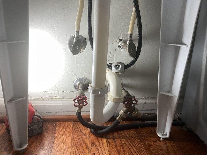 Responded to a water leak concern at a residential laundry area. Upon inspection, examined the washing machine shut-off valves and supply line connections located behind the appliance. Both hot and cold water supply valves with red handles were assessed for proper operation and leaks. Inspected the rubber supply hoses, wall-mounted connection points, and P-trap drainage configuration beneath the washer. Checked the utility sink plumbing and faucet assembly in the adjacent laundry area for any related leak sources. All connections were evaluated for integrity, and the water supply system was tested to ensure proper function and no active leaks were present at the time of inspection.