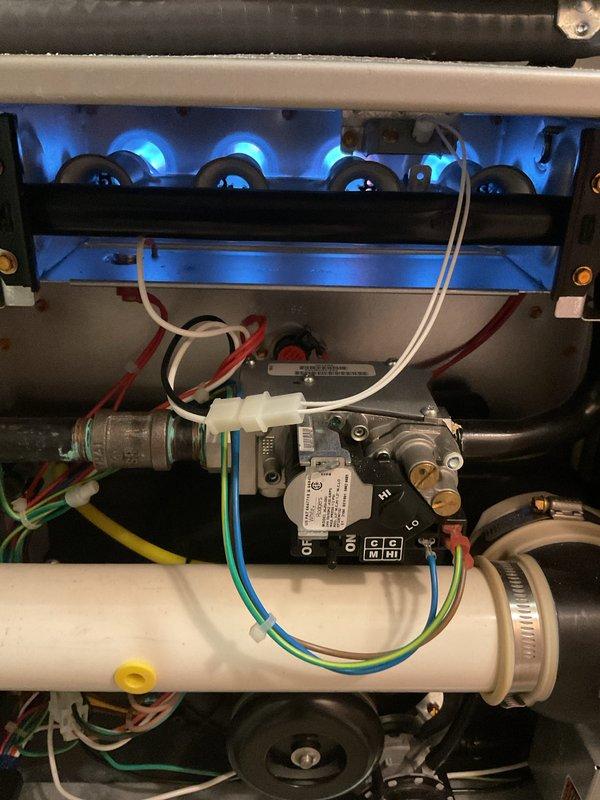 Completed comprehensive Gold Furnace Inspection on 5-year-old forced air heating system located on main floor. Performed full system evaluation including visual inspection of burner assembly, heat exchanger, gas valve controls, and electrical connections. Verified proper burner ignition and flame characteristics—all burners firing with appropriate blue flame pattern. Inspected air filter condition, noting moderate dust accumulation on mesh material within housing unit. Examined all wiring connections including control circuits, confirming secure attachment of red, white, blue, yellow, and green wires to gas valve assembly. Checked condensate drain system and PVC piping for proper operation and secure connections with metal hose clamps. Evaluated overall equipment operation and confirmed system is functioning within normal parameters. Unit operational and heating properly at time of inspection.