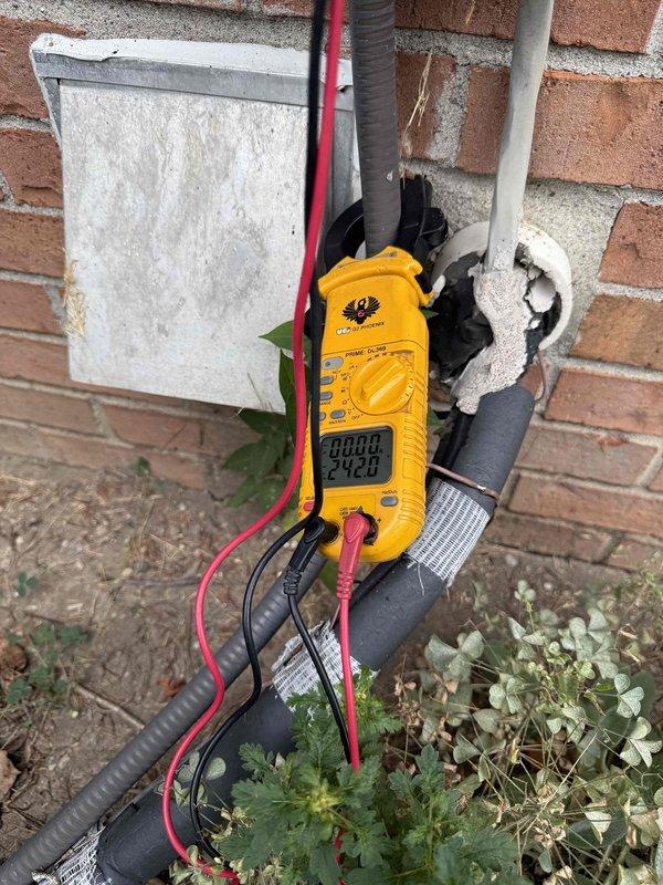 # HVAC Service Completed

Responded to no-cooling complaint affecting entire residence with 25-year-old air conditioning system. Condenser unit located at rear exterior of property.

Upon arrival, performed visual inspection of outdoor condensing unit and associated electrical components. Discovered severe fire damage to exterior electrical disconnect box mounted on brick wall near condenser. Interior of disconnect showed extensive charring, burned components, and heat damage to internal surfaces. Damage indicated electrical failure or short circuit event that compromised power supply to AC system.

Used digital multimeter to verify electrical readings and confirm loss of power at disconnect location. Tested voltage at various points in electrical circuit to isolate failure point. Black test leads documented voltage measurements at damaged disconnect box.

Photographed damaged electrical disconnect box showing burned interior components and compromised enclosure. Documented condition o
