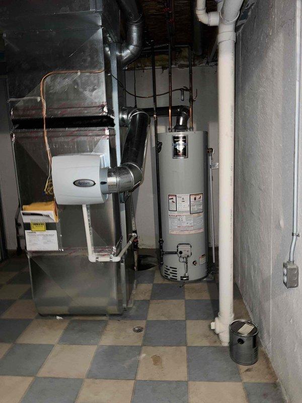 Completed Gold level furnace inspection on a 6-year-old forced air heating system located in basement. Performed comprehensive visual inspection of furnace cabinet, heat exchanger, burner assembly, and ductwork connections. Verified proper operation of all safety controls and limit switches. Inspected gas line connections and tested for leaks. Checked blower motor operation and belt condition. Examined flue pipe and venting system for proper installation and clearances. Confirmed adequate combustion air supply. Tested thermostat operation and system cycling. Inspected electrical connections and wiring. Verified proper drainage from condensate system. Unit operating within manufacturer specifications with no deficiencies noted. All safety systems functioning properly. Documented equipment condition with photos showing furnace installation with metal ductwork, adjacent water heater, and basement utility area setup.
