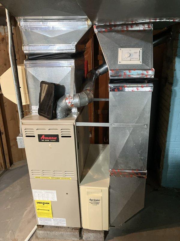 Conducted comprehensive inspection and assessment of 20-year-old Amana furnace system located in basement for certificate of occupancy requirements. Evaluated existing HVAC equipment including furnace unit, ductwork connections, humidifier, thermostat, and hot water tank to determine system condition and replacement needs. Documented current installation featuring cream-colored Amana furnace with galvanized metal ductwork, flexible duct connections, and electrical panel configuration to provide detailed replacement estimate for aging equipment prior to property sale.