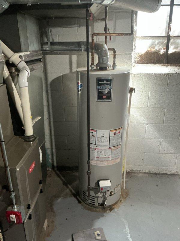 Completed Gold Furnace Inspection on a 10+ year old Lennox forced air furnace located in the basement. Unit is operational and homeowner confirmed equipment is working properly. Inspected furnace components, burners, heat exchanger, blower assembly, and safety controls per Gold maintenance protocol. Checked air filter, verified proper airflow, and tested thermostat operation. Examined venting system including PVC condensate drain lines for proper drainage and clearances.

During inspection, observed a Bradford White water heater adjacent to the furnace showing signs of water leakage at the base. Noted rust-colored staining on concrete floor extending from water heater base, indicating active or recent water discharge. Visible moisture trails and corrosion present at tank base where unit meets floor. Water heater control assembly with Honeywell components shows electrical connections intact, though the brass-colored relief valve area exhibits signs of discharge. Documented conditions wi