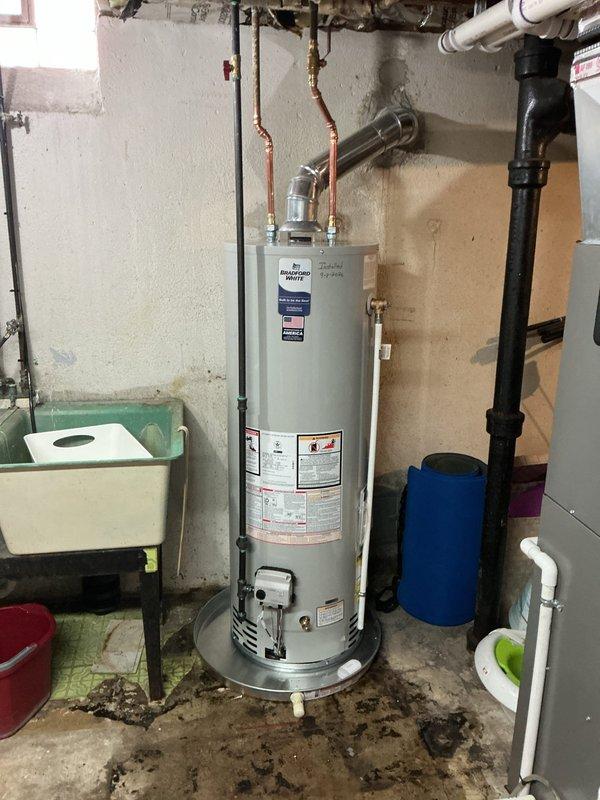 Responded to a leaking water heater in a basement laundry room. Removed and replaced the failed unit with a new 40-gallon residential tank-style water heater. Installation included proper copper piping connections with brass shut-off valves, installation of a drain pan beneath the unit for leak protection, and mounting of a water alarm system within the pan to provide early detection of future leaks. All plumbing connections were secured and tested for proper operation. The new water heater was positioned in the existing location, with supply and discharge lines properly connected to the overhead plumbing system. System was filled, pressurized, and verified for proper temperature settings and leak-free operation before completion.