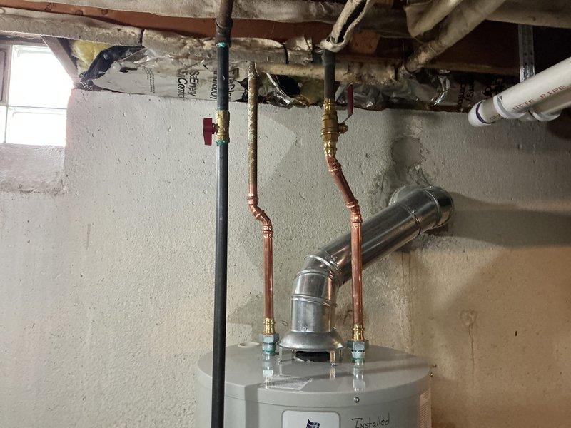Responded to a leaking water heater in a basement laundry room. Removed and replaced the failed unit with a new 40-gallon residential tank-style water heater. Installation included proper copper piping connections with brass shut-off valves, installation of a drain pan beneath the unit for leak protection, and mounting of a water alarm system within the pan to provide early detection of future leaks. All plumbing connections were secured and tested for proper operation. The new water heater was positioned in the existing location, with supply and discharge lines properly connected to the overhead plumbing system. System was filled, pressurized, and verified for proper temperature settings and leak-free operation before completion.