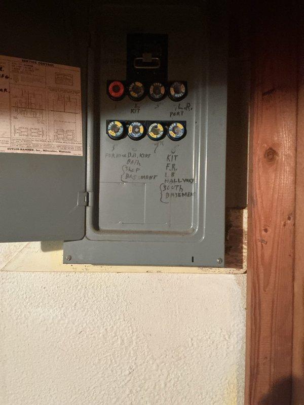 Responded to emergency call for damaged electrical service caused by fallen tree that displaced exterior electrical box from home. Assessed basement electrical panel located near furnace and water heater with less than 10 feet clearance. Panel showed functional interior components with multiple circuit knockouts and handwritten labeling system. Documented existing panel condition and clearance constraints for breaker box replacement requirements necessitated by exterior damage to main electrical service connection.