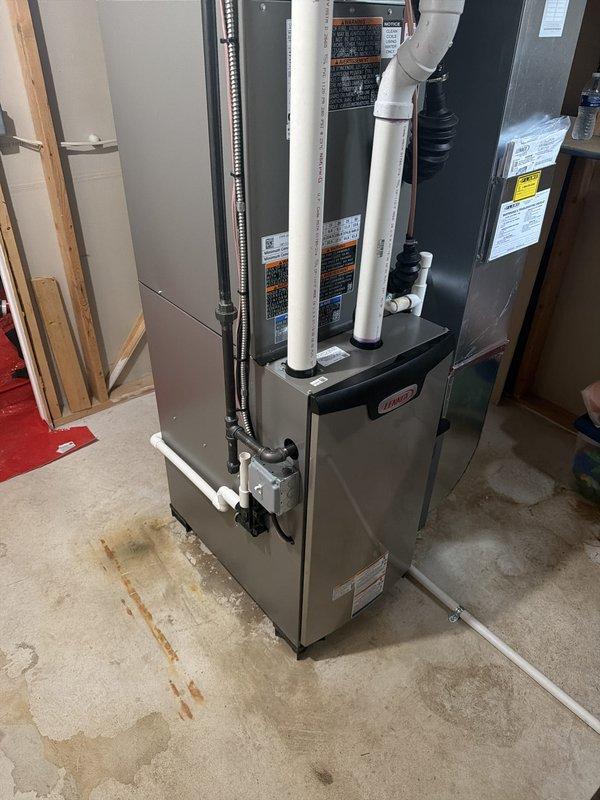 Completed full HVAC system installation including new furnace and air conditioning unit in basement utility area. Installed gray metal furnace cabinet with dual white PVC intake and exhaust venting pipes extending vertically from unit top, connected black flexible ductwork to system, and positioned equipment on concrete floor pad. Mounted exterior condensing unit on building exterior adjacent to electrical meter installation. Completed all necessary ductwork connections, refrigerant line installation, and electrical hookups to service panel. Verified proper drainage, tested system operation for heating and cooling cycles, and confirmed all safety controls functioning correctly. Submitted permit application for inspection approval. Completed manufacturer paperwork and registered equipment warranties. Customer qualified for utility rebate program and manufacturer rebate program based on high-efficiency equipment specifications.