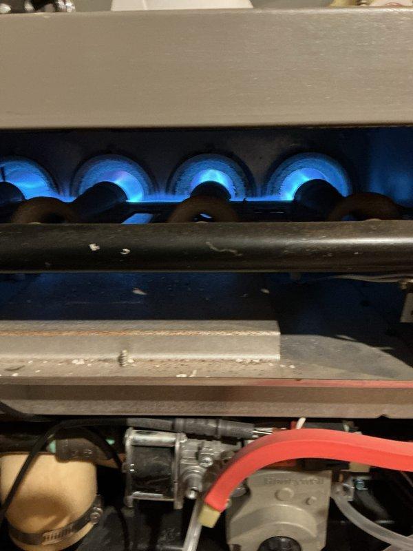 Completed comprehensive Gold Furnace Inspection on a gas-fired forced air heating system located in basement. Unit is over 10 years old and operational at time of service. Performed thorough inspection of all system components including burner assembly, heat exchanger, gas valve, and controls. Verified proper burner ignition and flame characteristics - observed clean blue flame pattern indicating efficient combustion. Inspected integrated Aprilaire humidifier mounted to ductwork system and verified connections. Evaluated galvanized ductwork configuration and flexible duct connections throughout the system. Documented existing condensate drain box condition on side of furnace, which homeowner reported as leaking and requested replacement during this fall heating inspection. Captured photographic documentation of active burner operation showing proper flame rollout and internal component condition, as well as overall system configuration including humidifier integration and ductwork layo