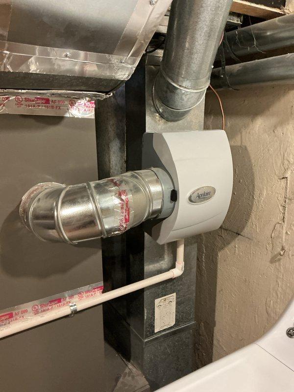 Completed comprehensive Gold Furnace Inspection on a gas-fired forced air heating system located in basement. Unit is over 10 years old and operational at time of service. Performed thorough inspection of all system components including burner assembly, heat exchanger, gas valve, and controls. Verified proper burner ignition and flame characteristics - observed clean blue flame pattern indicating efficient combustion. Inspected integrated Aprilaire humidifier mounted to ductwork system and verified connections. Evaluated galvanized ductwork configuration and flexible duct connections throughout the system. Documented existing condensate drain box condition on side of furnace, which homeowner reported as leaking and requested replacement during this fall heating inspection. Captured photographic documentation of active burner operation showing proper flame rollout and internal component condition, as well as overall system configuration including humidifier integration and ductwork layo