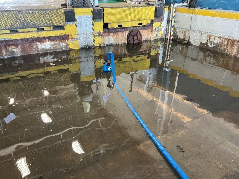 Completed sump pump installation at commercial loading dock facility experiencing significant water accumulation. Installed new sump pump system in concrete basin with deteriorated walls showing extensive water damage and rust staining. Routed discharge line through flooded area to manage standing water conditions throughout the loading bay and warehouse space.