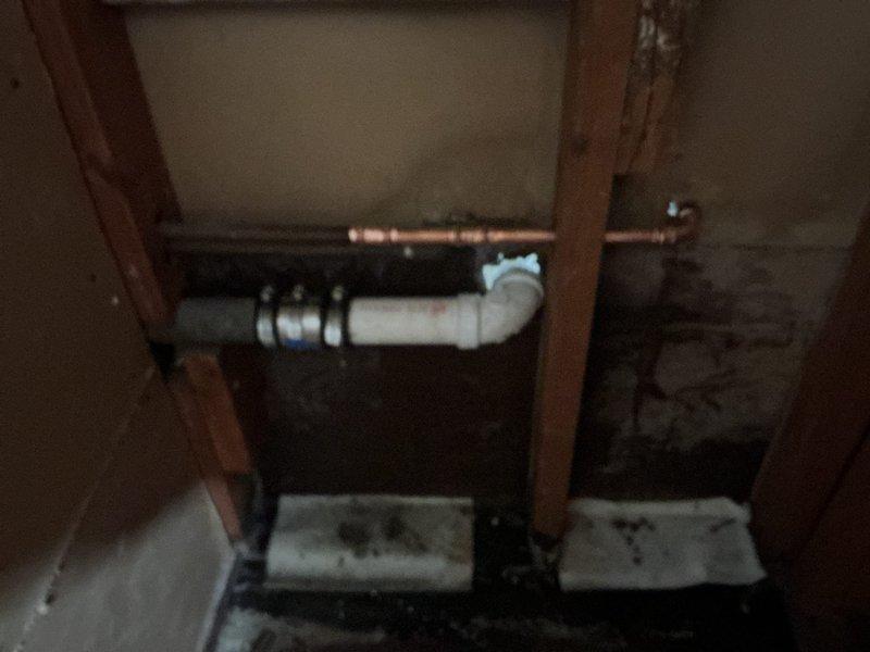Responded to active water leak dripping from bedroom ceiling light fixture onto bed. Traced leak source to deteriorated plumbing fitting in second-floor bathroom directly above affected bedroom. Upon investigation, identified compromised pipe connection with visible corrosion on copper supply line and deteriorated PVC piping showing weathered surfaces and rough texturing. Repaired faulty fitting, secured all connections, and verified water supply system integrity. Leak has been stopped at the source. Customer advised that ceiling and electrical fixture may require separate repair due to water intrusion damage.