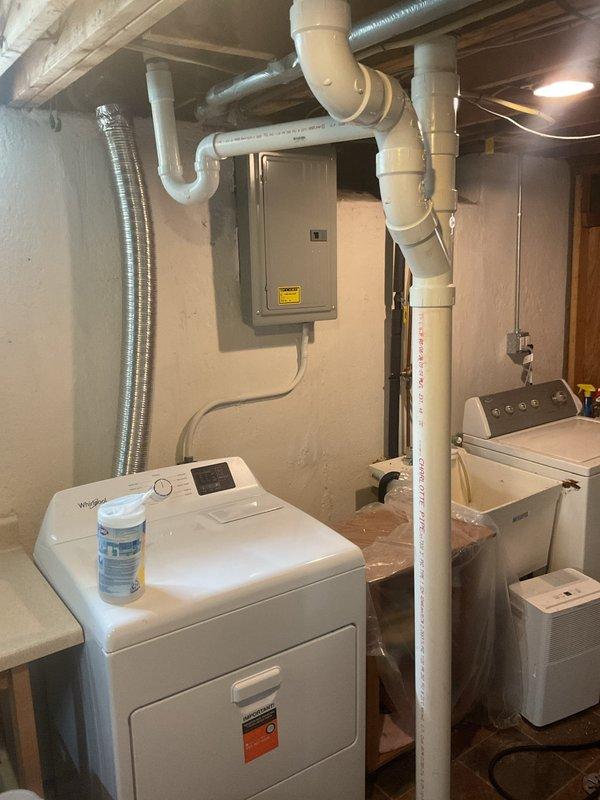 Completed installation of new PVC drainage system in basement utility area, including vertical stack pipe with multiple elbow joints and horizontal ceiling-mounted drainage lines. All connections were properly fitted and secured to existing plumbing infrastructure to ensure proper water flow from laundry equipment.