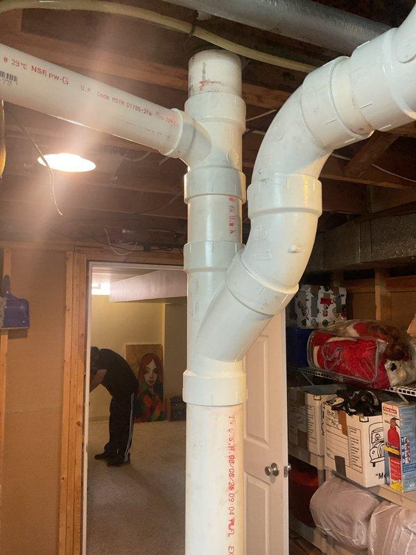 Completed installation of new PVC drainage system in basement utility area, including vertical stack pipe with multiple elbow joints and horizontal ceiling-mounted drainage lines. All connections were properly fitted and secured to existing plumbing infrastructure to ensure proper water flow from laundry equipment.
