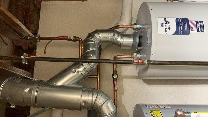 Responded to service call regarding water heater tank leak at side joint connection. Upon inspection, identified active leak at threaded pipe joint on water heater assembly. Documented existing installation configuration including dual water heater setup with associated copper supply lines, galvanized vent piping, pressure relief valve, and shut-off valves. Captured photographic evidence of leak location and overall system condition for warranty recall documentation. Customer advised to contact manufacturer customer service line for recall verification and resolution procedures.