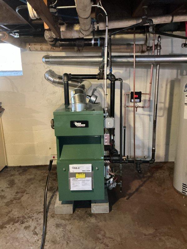 Completed full installation of Weil-McLain CG5-C residential boiler system in basement mechanical room. Installed new green boiler unit on concrete block base with complete piping configuration including supply and return lines, black metal piping with elbow connections, pressure gauge, control valves, and safety devices. Connected cylindrical expansion tank and integrated copper piping with shut-off valves and monitoring controls. Established all mechanical and electrical connections including flexible conduit, relay controls, and power supply. Requested mechanical, electrical, and boiler permits for system reconnection and final inspection.