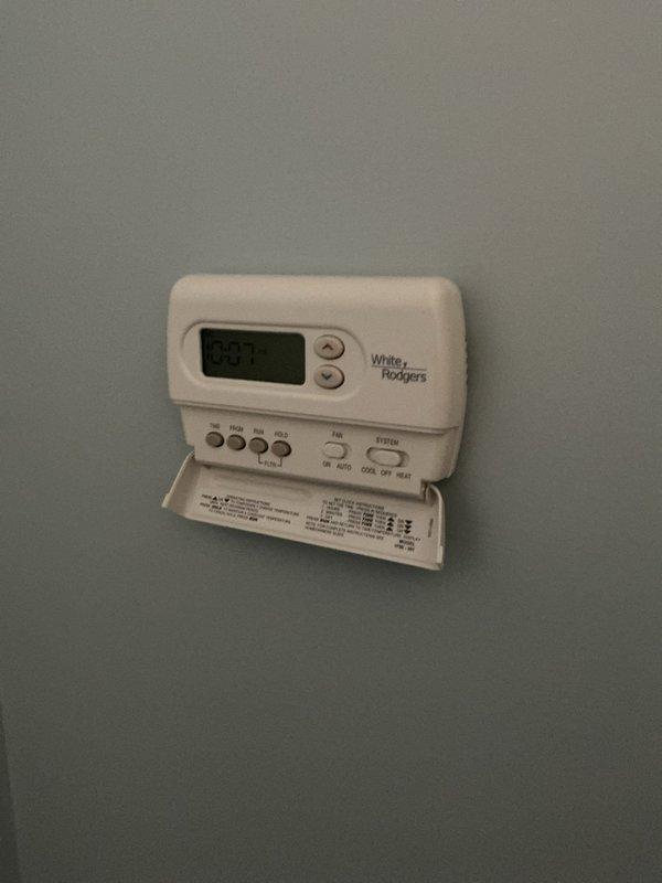 Responded to service call for reported condenser leak at upstairs unit. Upon arrival, performed visual inspection of outdoor condenser unit and indoor thermostat system. Assessed 10-15 year old HVAC system for potential drip pan failure and evaluated overall unit condition. Documented equipment with photos showing exterior condenser placement and indoor White-Rodgers programmable thermostat displaying current temperature reading of 83 degrees.