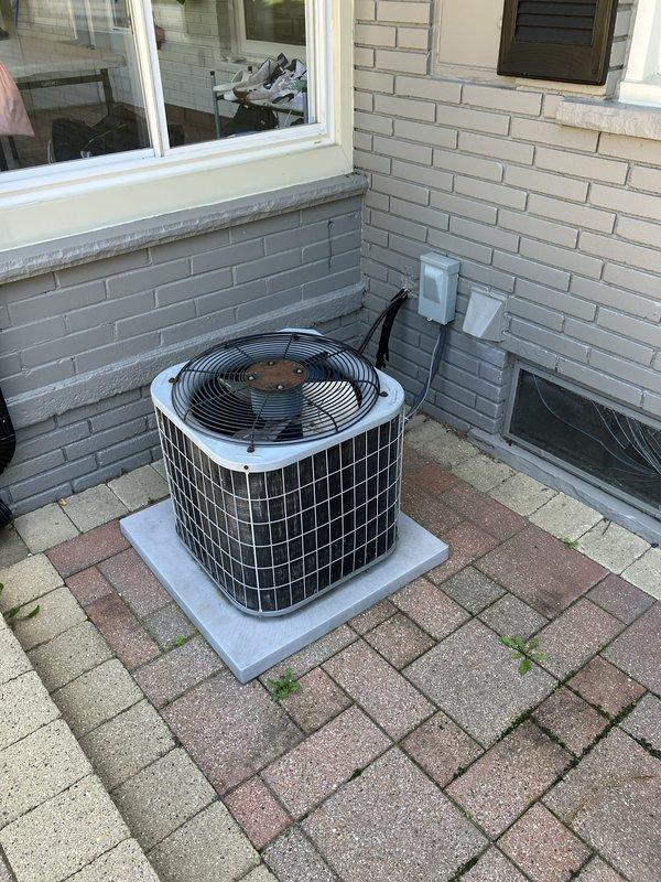 Conducted on-site evaluation for complete HVAC system replacement at residential property with 20-year-old equipment operating at minimal capacity. Assessed existing outdoor condensing unit positioned on concrete pad against brick exterior wall with dual electrical disconnect boxes, along with natural gas furnace located in basement. Documented current system configuration, electrical connections, and installation conditions to provide comprehensive replacement estimate for new air conditioning and heating equipment.